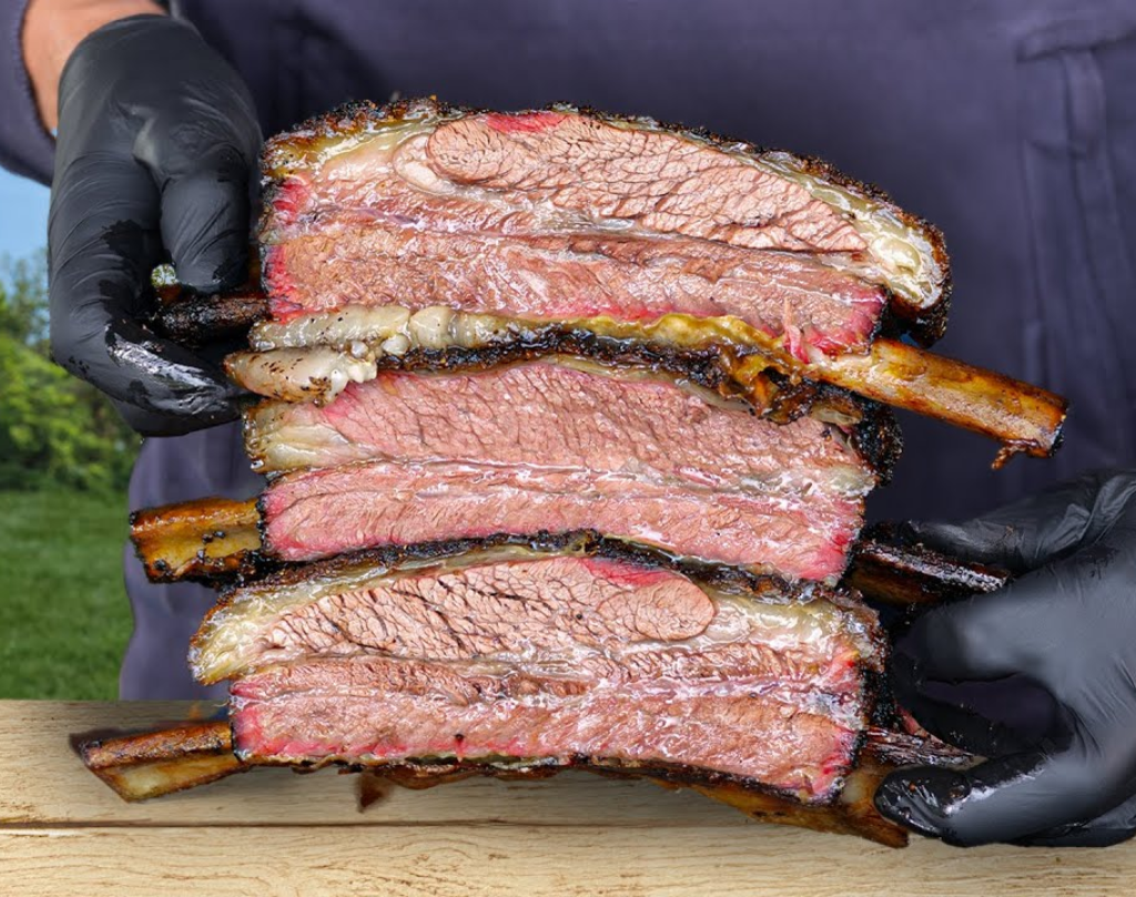 Man houd 3 stukken beef ribs vast na heerlijke bereiding. Is een echte BBQ fanaat.